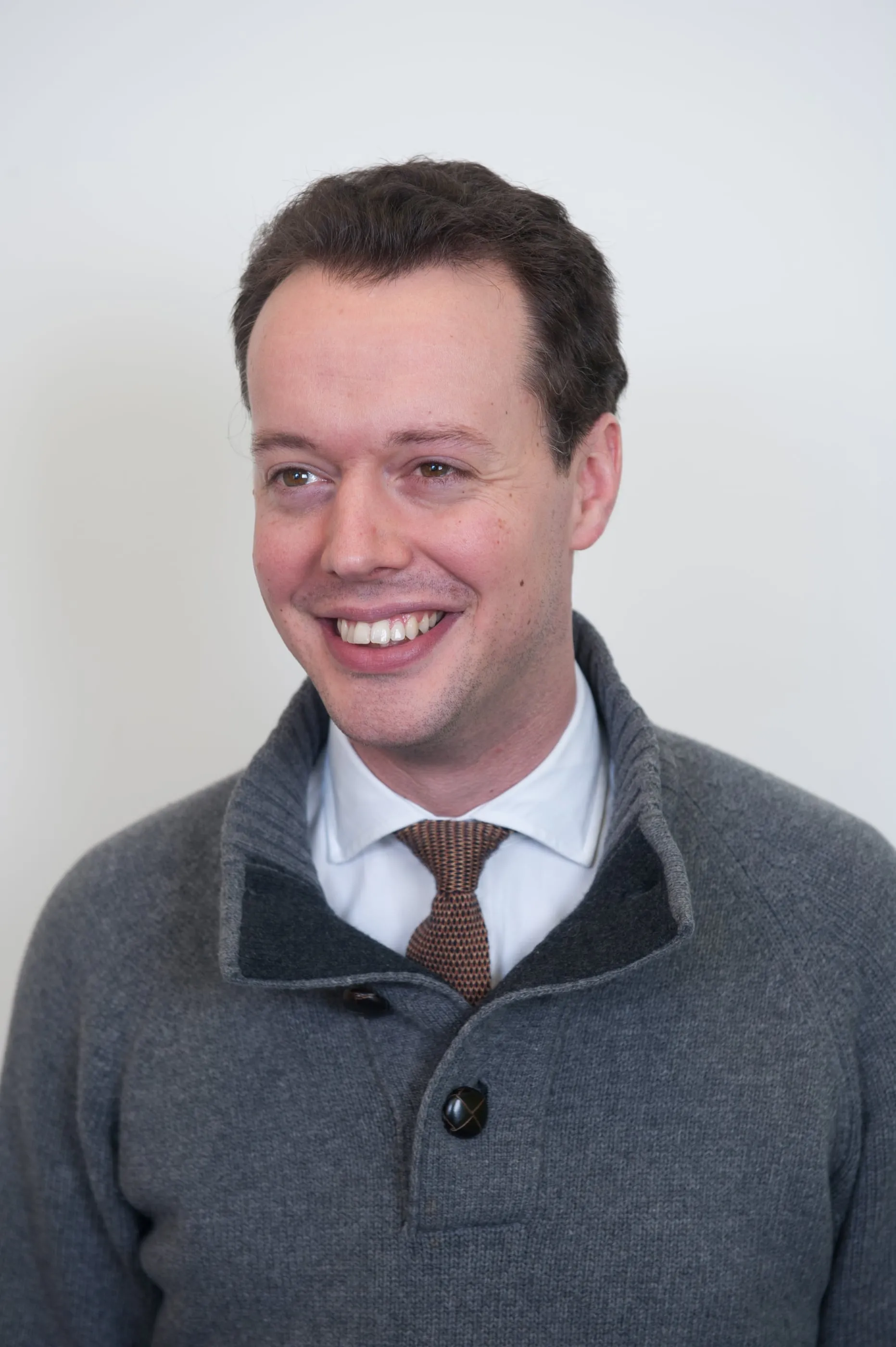 Corporate headshot of a man in a jacket and tie against a light grey background