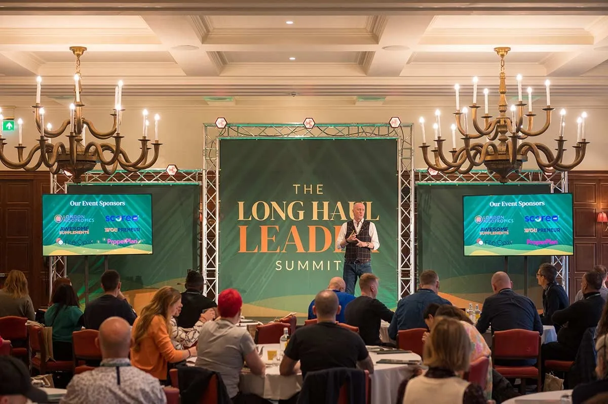 A summit stage and seated audience in a hotel ballroom