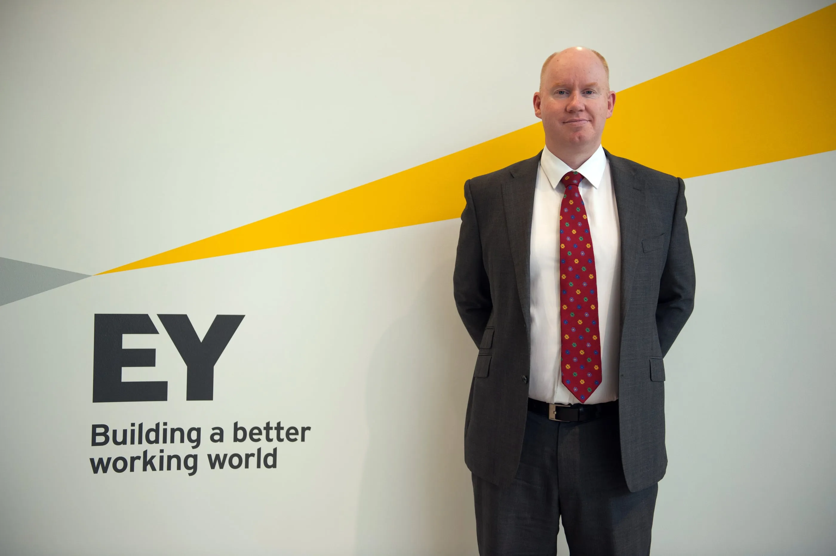 A man photographed in front of the EY sign at their Cambridge office