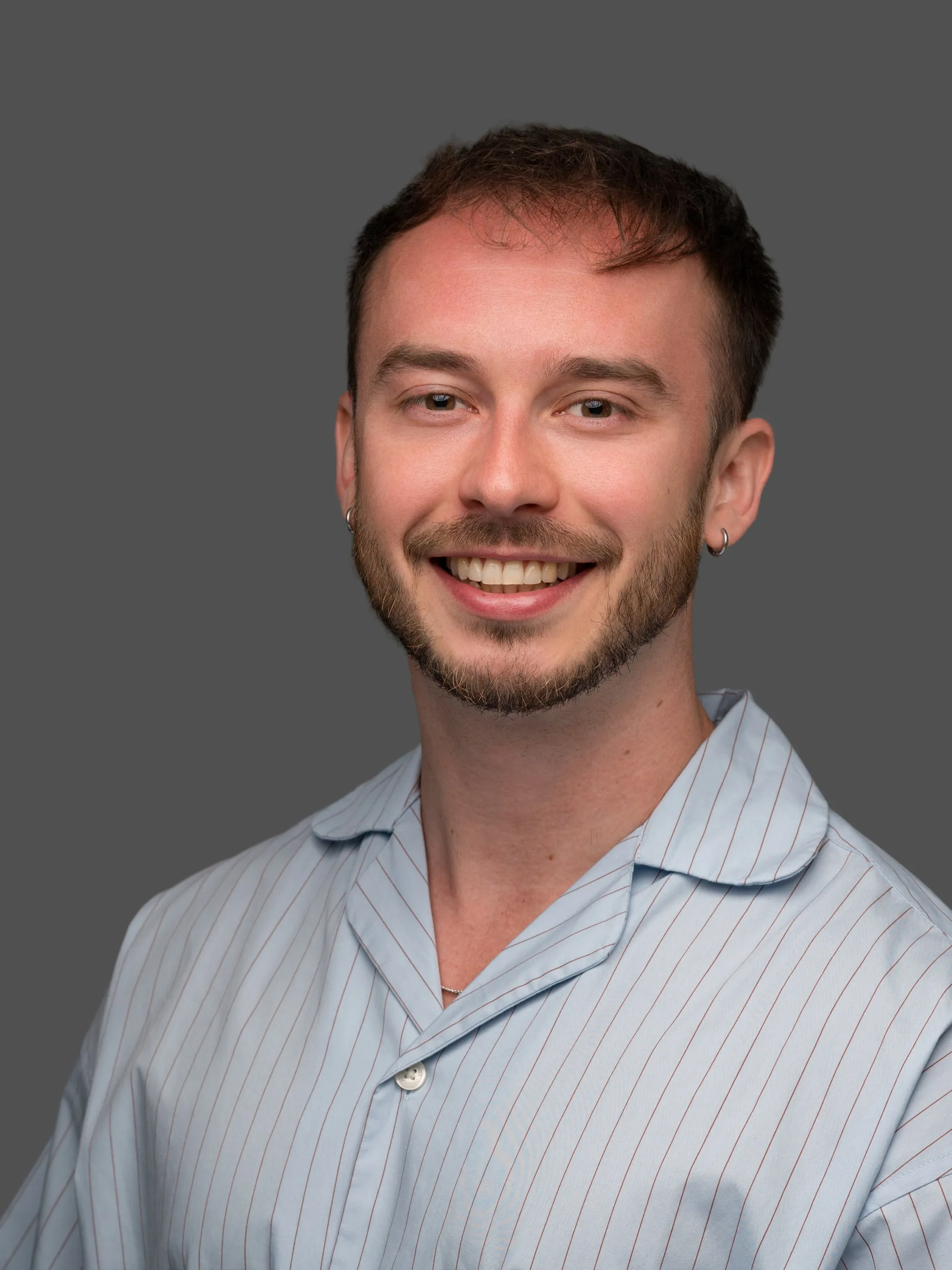 Corporate headshot of a man in a striped shirt on a grey background