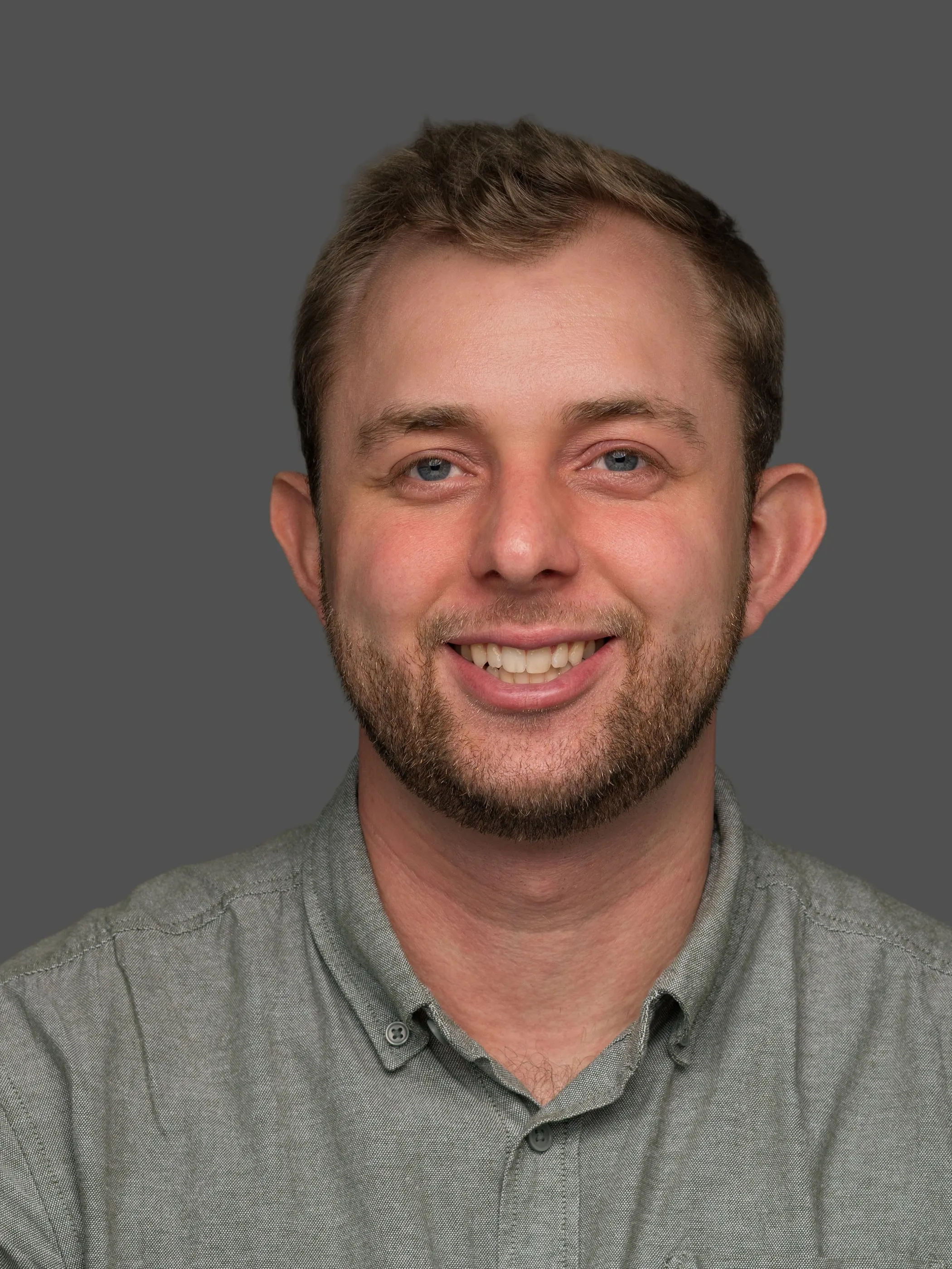 Corporate headshot of a man in a grey polo shirt on a grey background