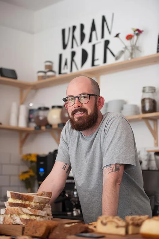 A man behind a cafe counter with bread and cakes in front of him